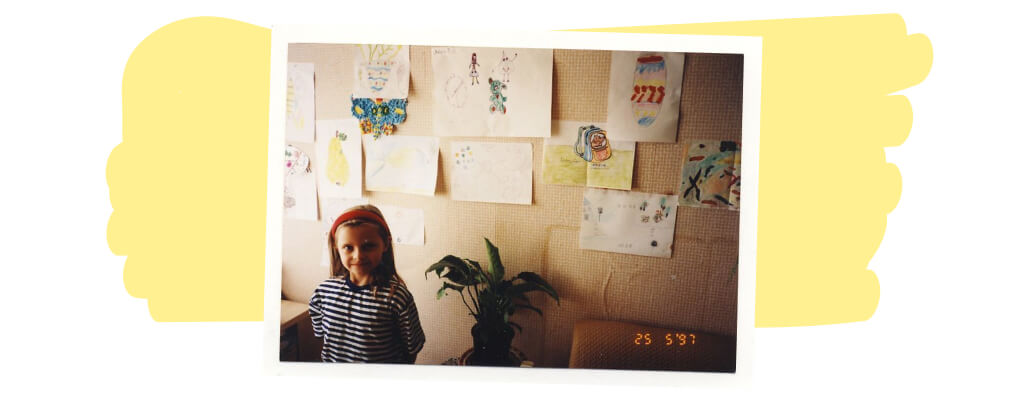 autorka w wieku 8 lat na tle ściany z przyklejonymi pracami plastycznymi